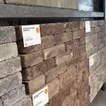 Showroomwand schuin gezien met bruine en grijze trommelstenen en label 20x5x7 Bruin