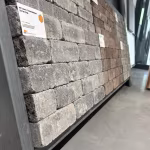 Showroomwand schuin gezien met grijze en bruine trommelstenen en artikellabels