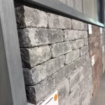 Zijaanzicht van opgestapelde getrommelde WG Stone steentjes in showroomrek naast bruine variant