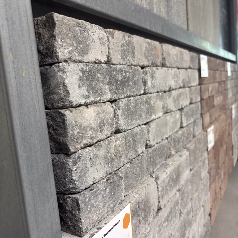 Zijaanzicht van opgestapelde getrommelde WG Stone steentjes in showroomrek naast bruine variant