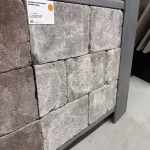 Close-up van getrommelde WG Stone Taupe stenen in showroomrek met label