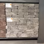 Showroomstaal WG Stone Trommelsteen 21x7x8 Taupe gestapeld in rek met artikellabel