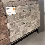 Showroomstaal WG Stone Trommelsteen 21x7x8 Taupe naast bruine stenen met leesbaar label