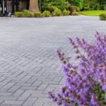 Brede oprit van BSS betonklinkers 8 cm in visgraatverband met paarse bloemen
