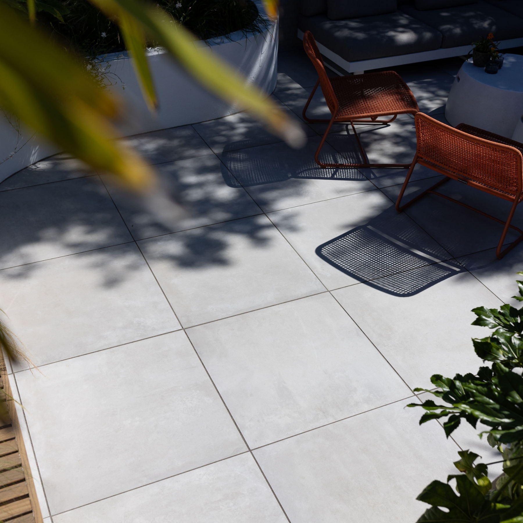 Lichtgrijze keramische terrastegels met oranje stoelen en plantenbak