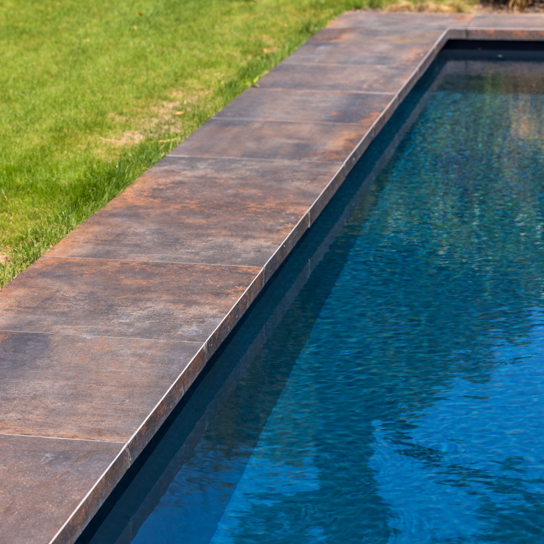 Keramische tegels in roestlook rondom zwembad met helder blauw water