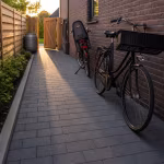 Antraciet betonklinkers 8 cm als smal pad langs bakstenen gevel met fiets in avondzon