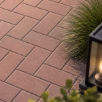 Close-up van roodbruine betonklinkers 8 cm Heide in visgraat met siergras en tuinlamp