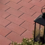 Close-up van rode betonklinkers met zwarte lantaarn en groene struik op de voorgrond